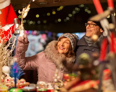 shopping, winter holidays and people concept - happy senior couple at christmas market souvenir shop on town hall square in tallinn, estonia