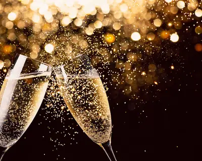 Two glasses of champagne toasting in the nigh with lights bokeh, glitter and sparks on the background