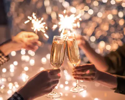 Hands of couple clinking with flutes of champagne and their friends holding sparkling bengal lights