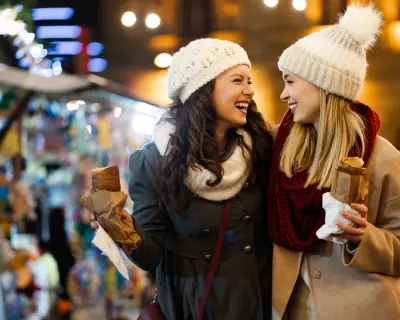 Happy women friends enjoying christmas market and having fun together outdoors. Holiday travel people concept