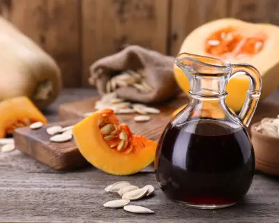 Fresh pumpkin seed oil in glass jug on wooden table. Space for text