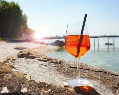 Cold aperol spritz cocktail at the lakeshore in summer. Horizontal close-up.